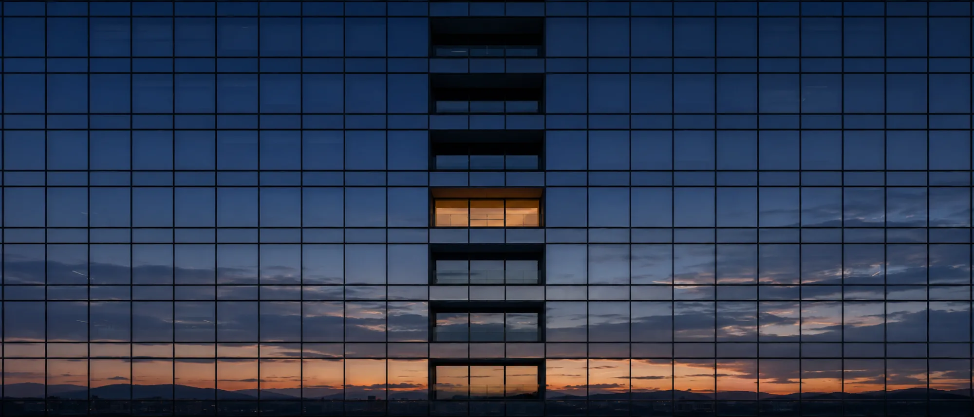 Glass office facade at dusk with a single window still lit