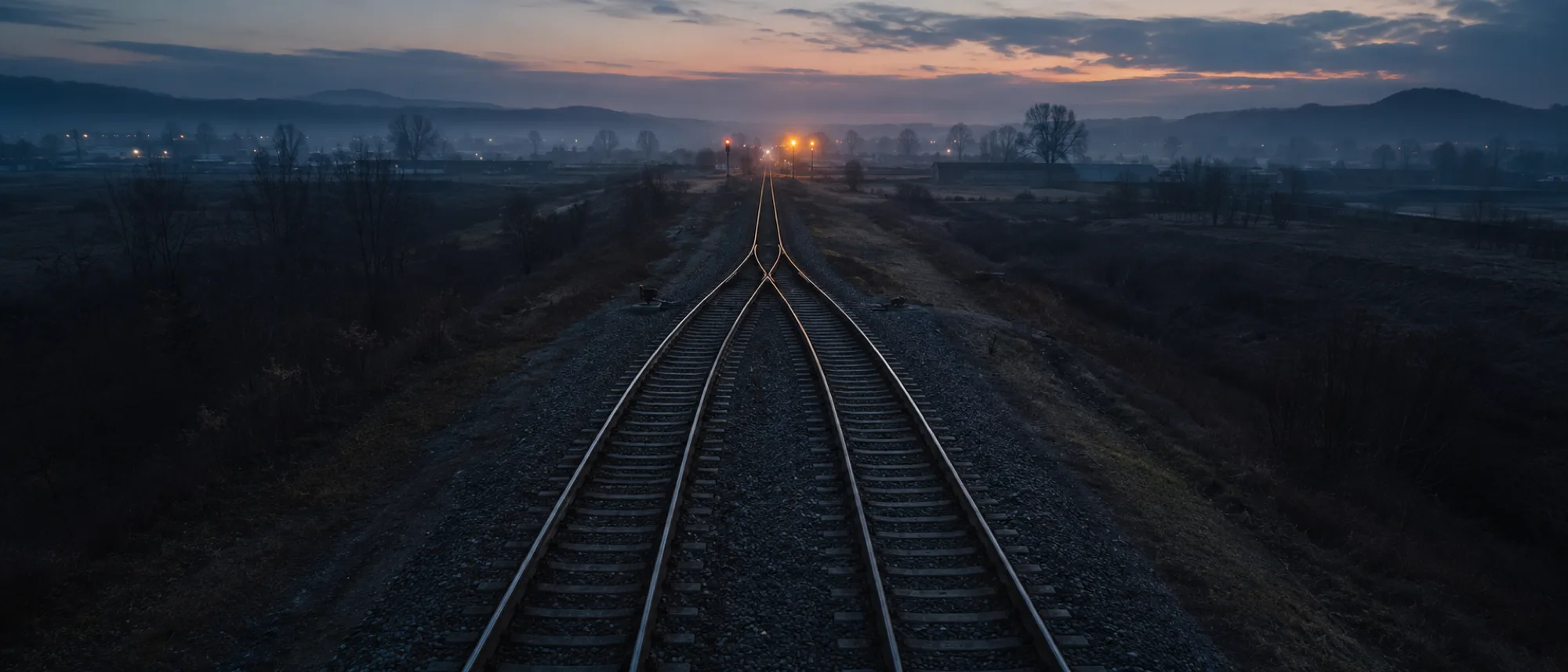 Two railway tracks converging into one line at dusk