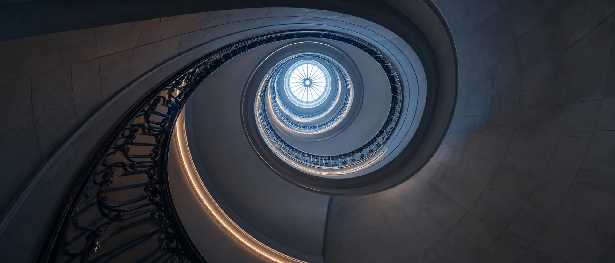 Spiral staircase seen from below, curving upward into light