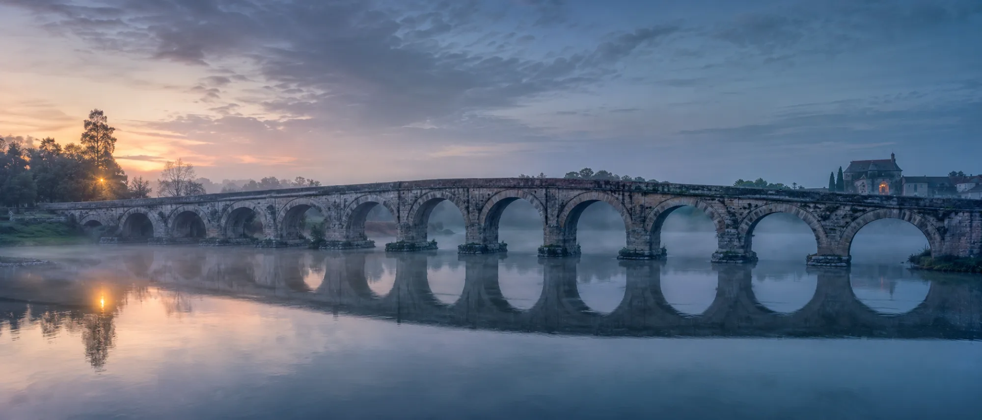 Old stone bridge standing over misty water at dusk