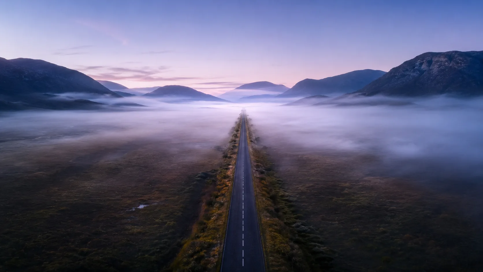 A straight road through clearing morning fog, the path ahead visible
